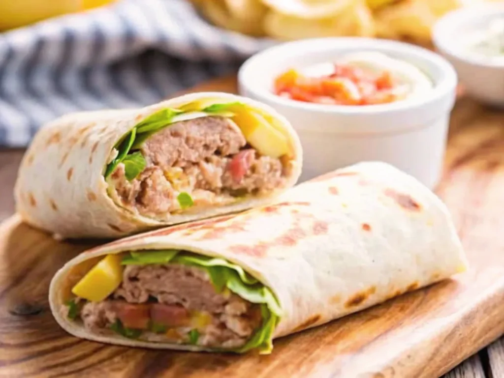 Close-up of two freshly made tuna wraps on a wooden serving board, showcasing a filling of tuna, fresh vegetables, and melted cheese. The wraps are paired with small bowls of salsa and creamy dipping sauces in the blurred background, adding a vibrant and inviting touch to the presentation.