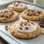 Close-up of homemade Crumbl-style cookies with thick, soft centers, topped with frosting and colorful toppings, arranged on parchment paper.