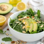 Bowl of spinach salad with lemon dressing, avocado, and almonds – vibrant and healthy side salad