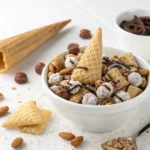 Bowl of Nutty Buddies coated in powdered sugar with chocolate and nuts on a white background – quick snack recipe