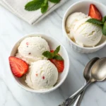 Scoop of cottage cheese protein ice cream with strawberry and mint in a small white bowl