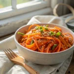 Close-up of vibrant *retinol carrot salad* ribbon curls with sesame-lime dressing in a white bowl.
