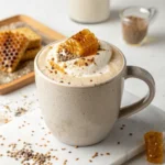 Recipe card photo of a salted tahini honeycomb latte in a neutral mug with honeycomb and sesame seeds — creamy, nutty, and visually stunning.