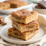 Stack of Chewy Snickerdoodle Cookie Bars on a white plate with golden cinnamon-sugar crust